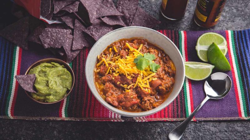 beef and kidney bean chili with guacamole, limes, and tortilla chips
