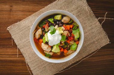 chicken and black bean soup in a white bowl with sour cream and avocado