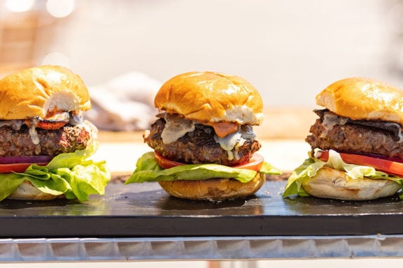 three beef cheeseburgers with lettuce and tomato on board