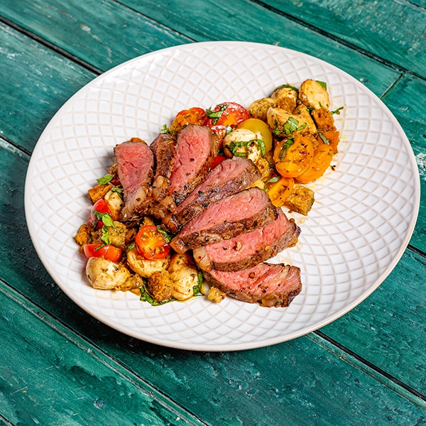 Steak surrounded by a bruschetta salad on a plate