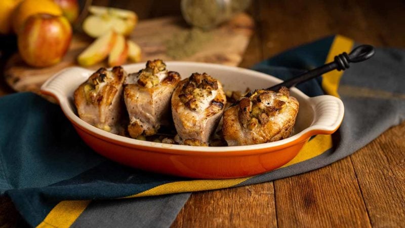 baked stuff pork chops in a dish next to apples