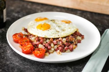 an egg on top of corned beef hash on a plate on top of a breakfast table