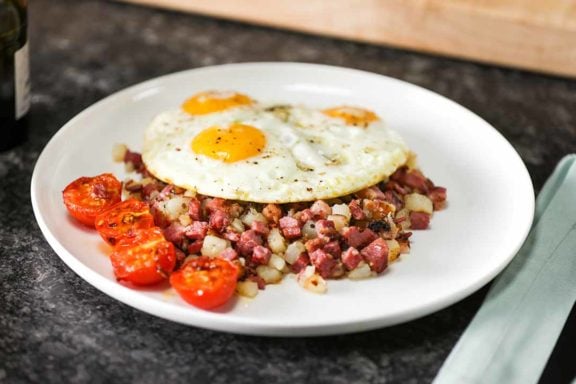 an egg on top of corned beef hash on a plate on top of a breakfast table