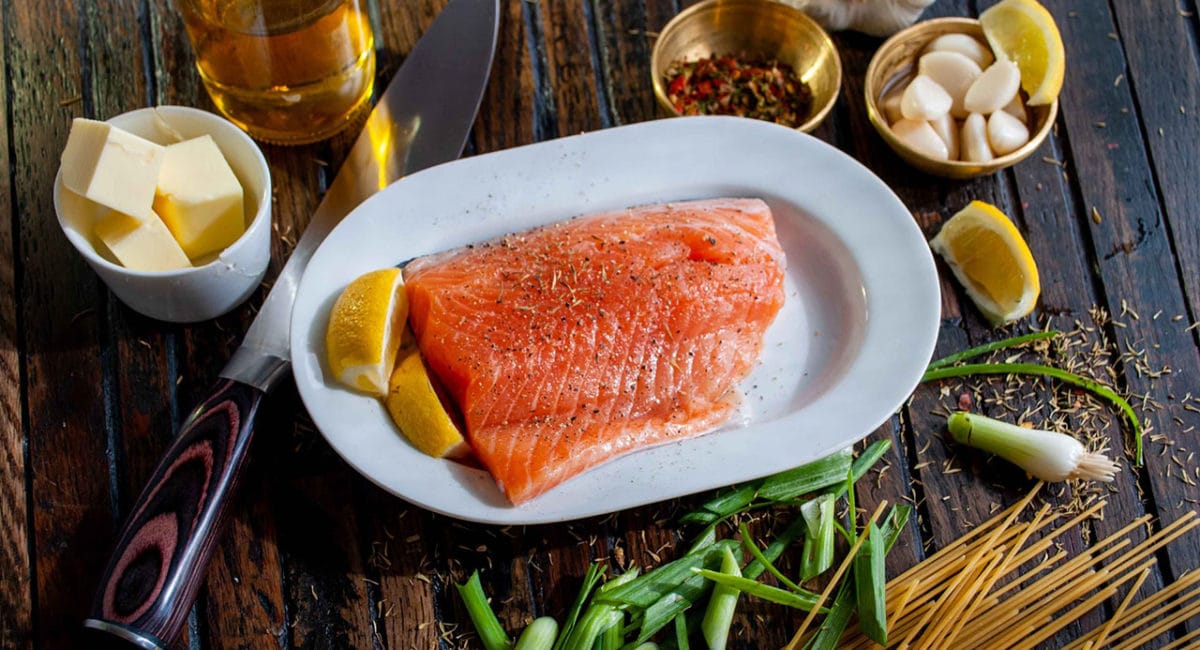 Raw salmon on a plate surrounded by ingredients to make a meal