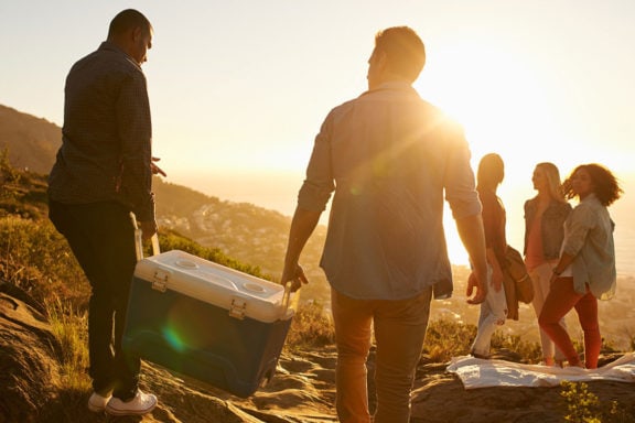 A group of people carrying a cooler with the sun shining