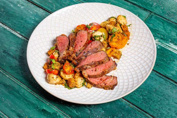 Steak surrounded by a bruschetta salad on a plate