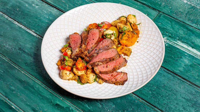 Steak surrounded by a bruschetta salad on a plate