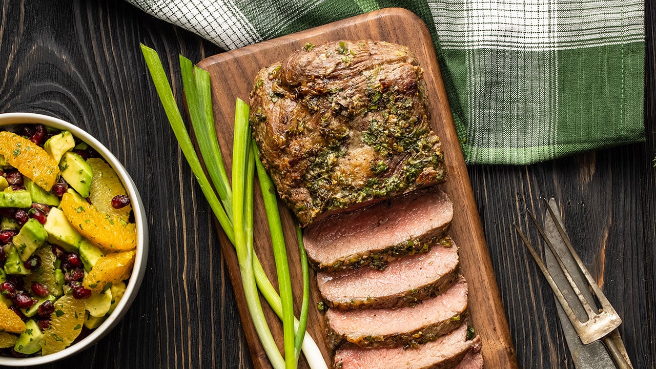 Tri-tip on a cutting board with a bowl of avocado pomegranate orange salsa on the side