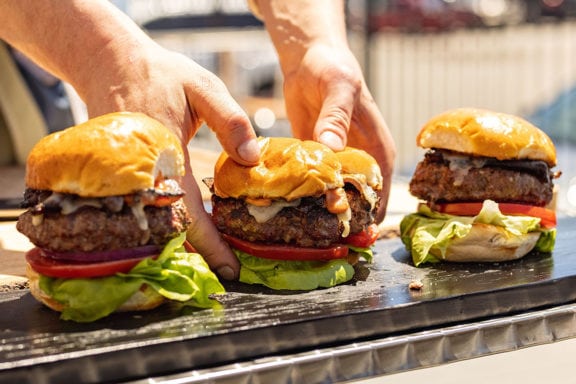 hands grabbing three bacon cheeseburgers