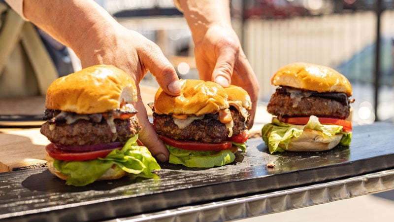 hands grabbing three bacon cheeseburgers