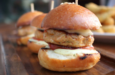 Three ground chicken sliders with condiments and cheese on a cutting board
