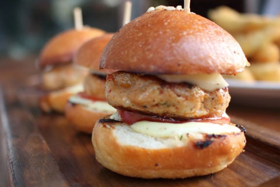 Three ground chicken sliders with condiments and cheese on a cutting board