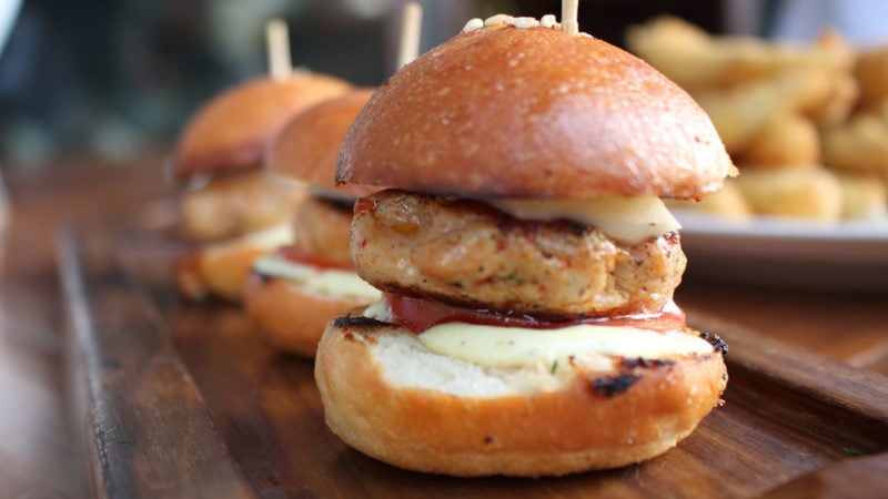 Three ground chicken sliders with condiments and cheese on a cutting board