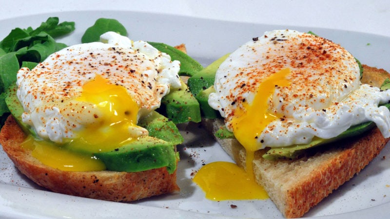 two slices of toast topped with avocado and poached eggs