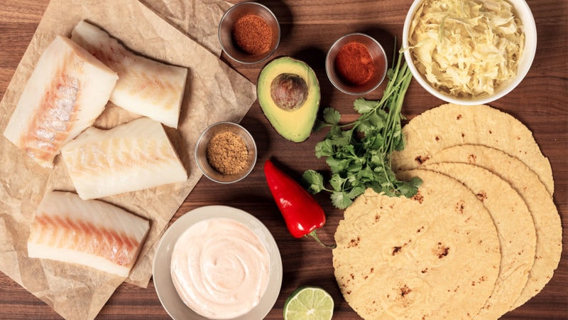 spices, avocado, cheese, tortillas, and defrosted cod laid out for tacos