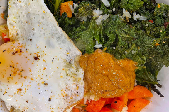 roasted kale, carrots, chili mayo, and a fried egg over crispy rice in a bowl