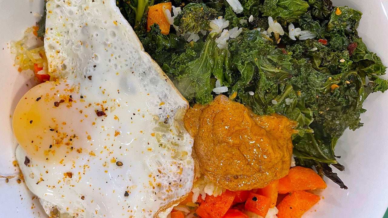 roasted kale, carrots, chili mayo, and a fried egg over crispy rice in a bowl