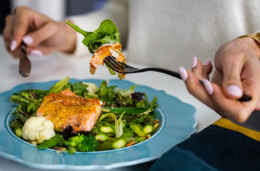 person eating salmon on top of vegetables with a fork and knife