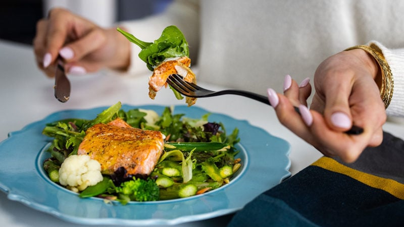 person eating salmon on top of vegetables with a fork and knife