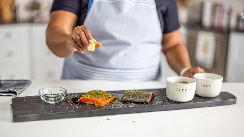 Person squeezing a lemon onto salmon filets on a cutting board with salt and pepper