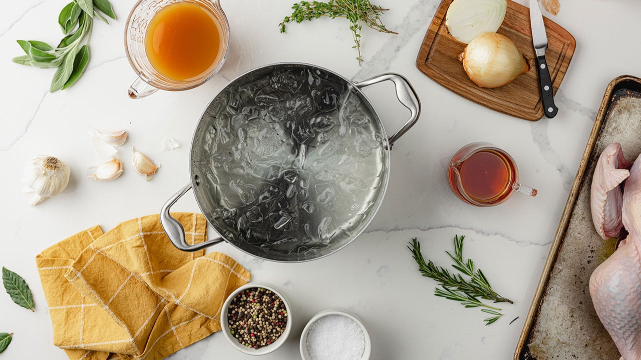 pot filled with ice water on a table next to seasonings, onions, a brine, and a raw turkey