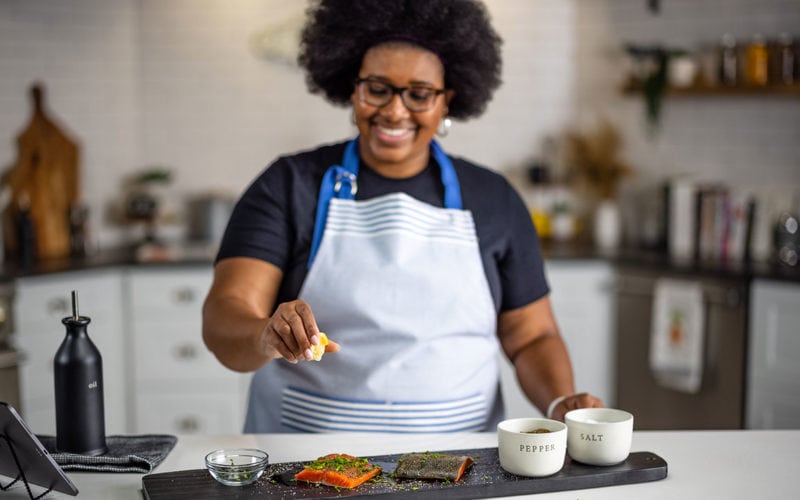 beginner cook in the kitchen following a recipe and squeezing lemon onto salmon filet